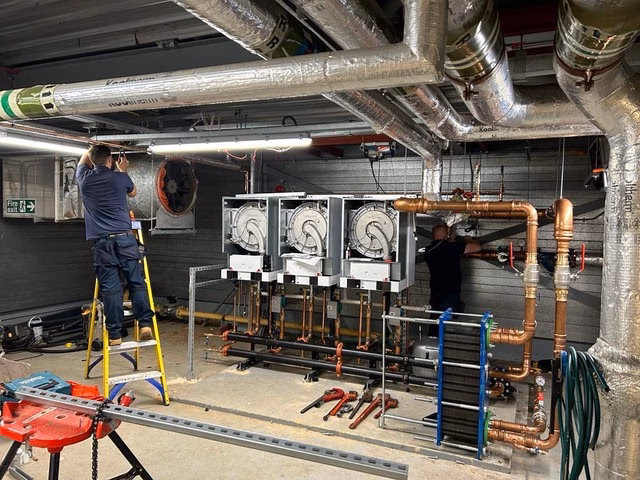 Engineers installing commercial HVAC and pipework system in plant room